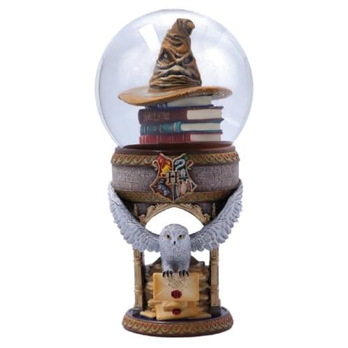 Bola de nieve con el Sombrero Seleccionador sobre libros apilados y Hedwig posada bajo un arco con el escudo de Hogwarts