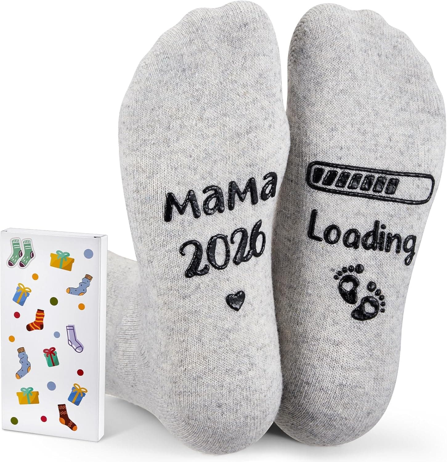 Las suelas de los dos calcetines grises: en una se lee «mamá 2026» con un corazón y en la otra una barra de carga con «loading» y dos huellas de pie de bebé, con la caja de regalo al lado