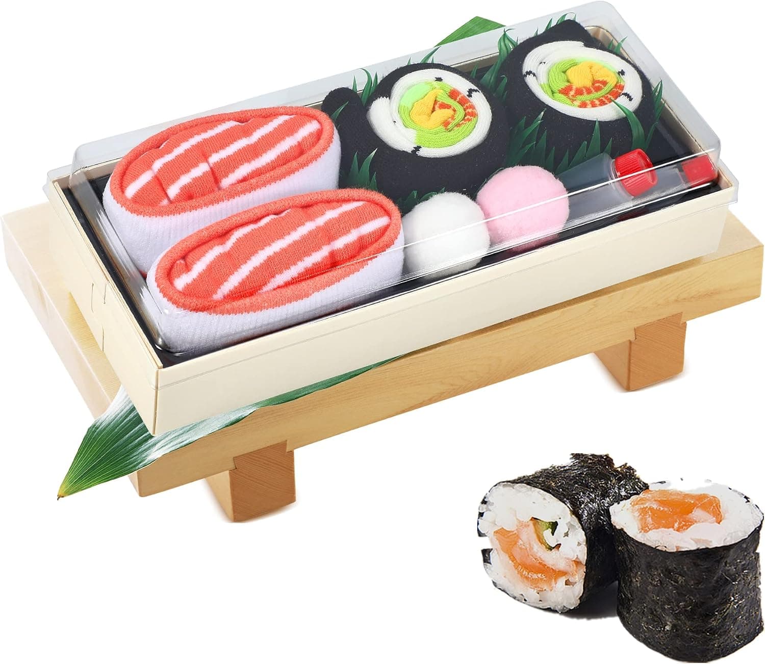 Bandeja transparente con calcetines doblados como piezas de sushi, dos nigiris de salmón y dos makis, sobre un soporte de madera con hoja de bambú