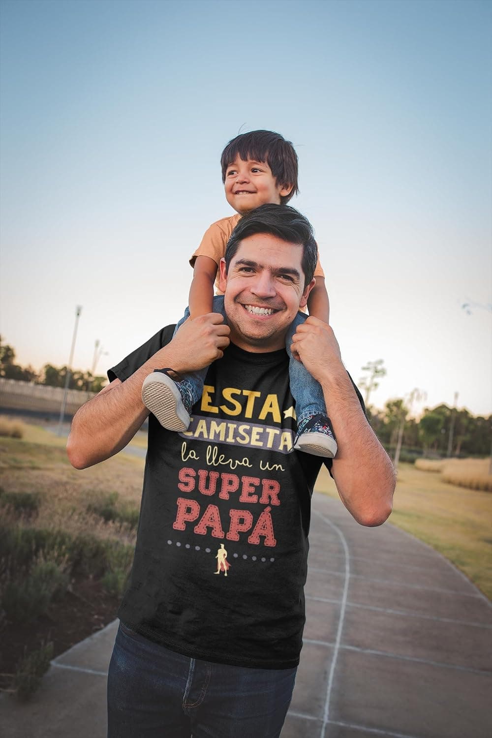 Padre con su hijo a hombros, luciendo una camiseta negra con el texto "Esta camiseta la lleva un Súper Papá"
