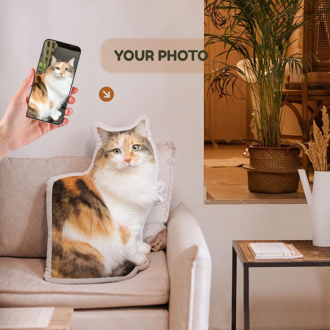 Un cojín con forma de gato atigrado sobre un sofá, junto al móvil con la foto original