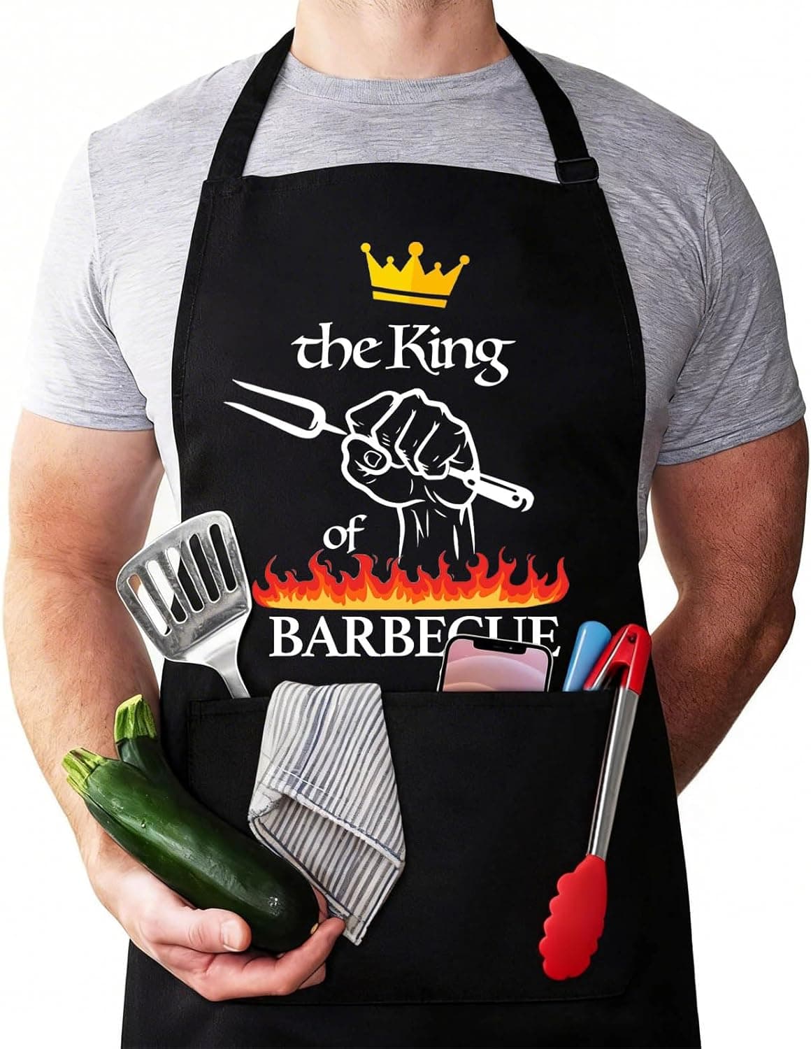 Un hombre con el delantal negro puesto, con la frase «the King of Barbecue» y una corona, y utensilios asomando por el bolsillo
