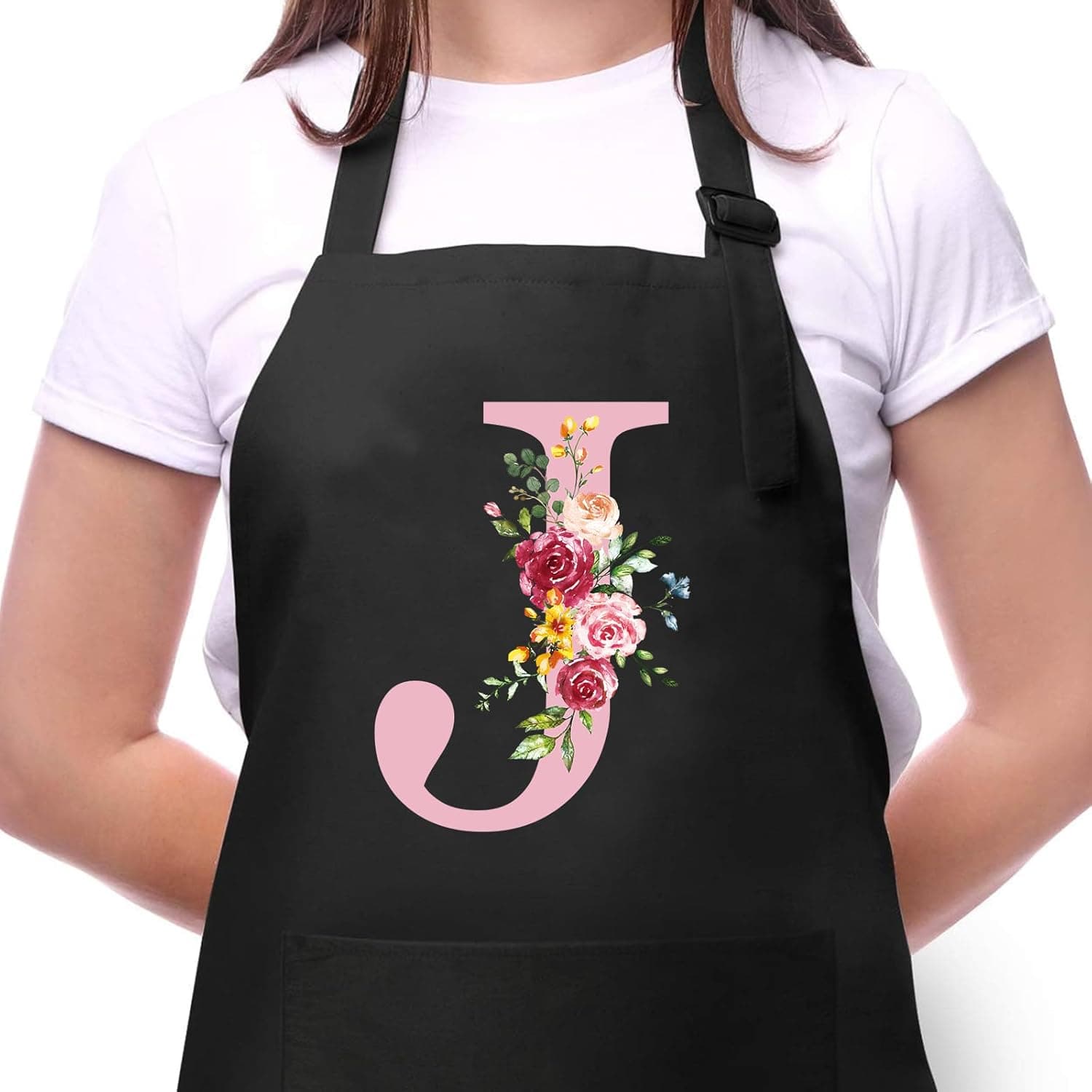 Delantal negro con una gran letra J rosa decorada con flores en tonos rojos, rosas y amarillos, sobre una mujer con camiseta blanca