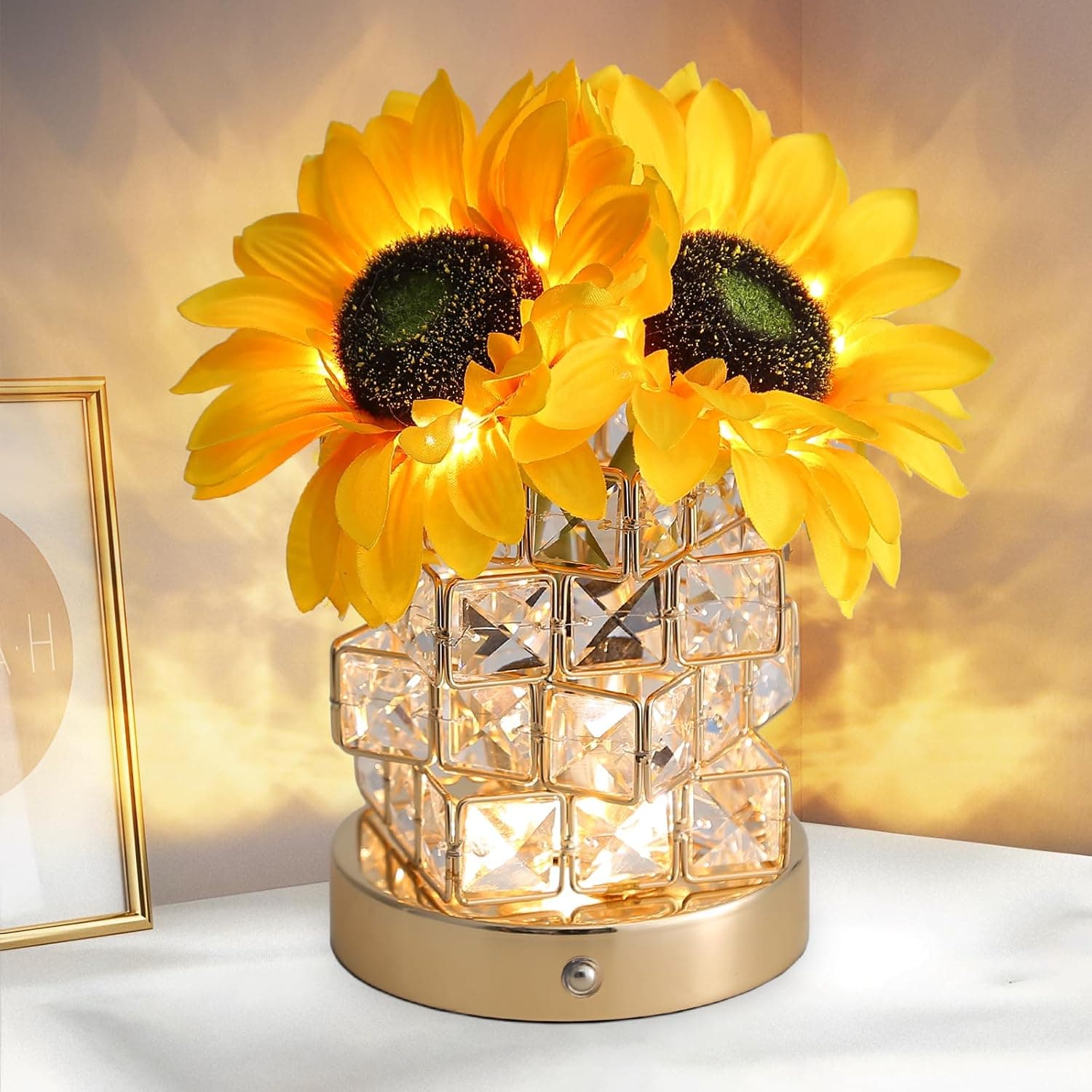 La lámpara encendida con dos girasoles dorados sobre una base de cristal tallado en cubos, con luz cálida