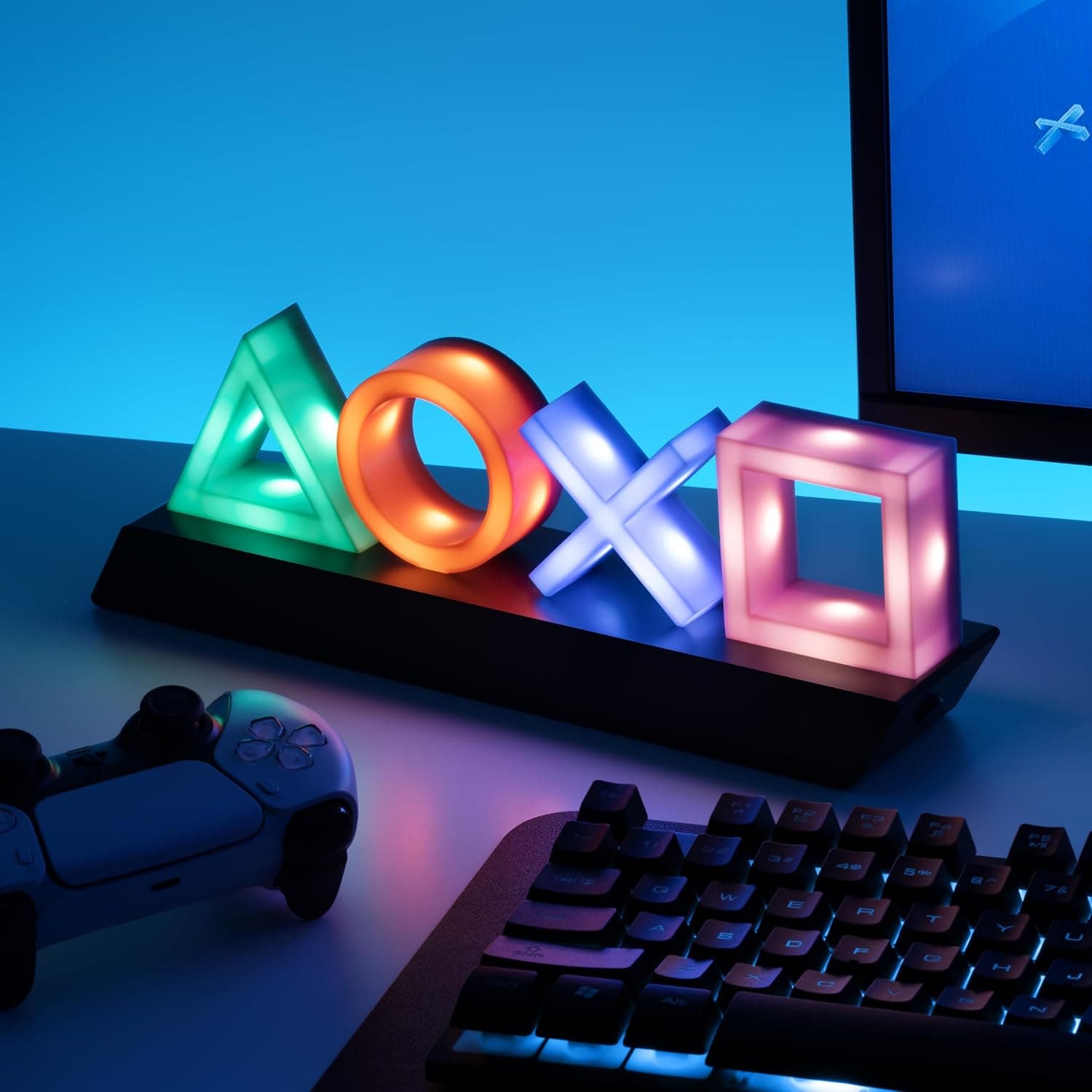 La lámpara encendida en un escritorio, junto a un teclado y un mando, con la pantalla al fondo