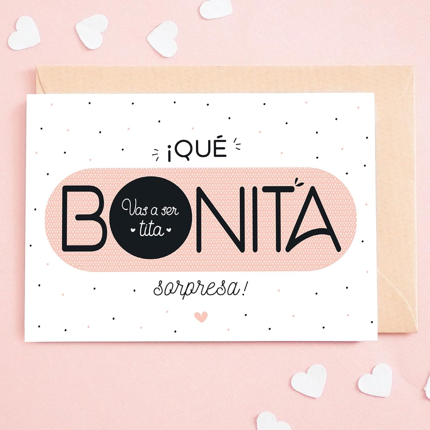 La tarjeta ya rascada sobre fondo rosa con confeti de corazones: en el hueco negro de la O se lee «vas a ser tita»