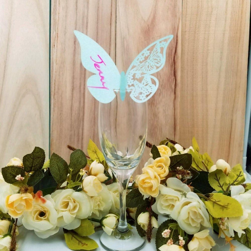 Mesa larga puesta para una boda con varias copas, cada una con su tarjeta mariposa colocada en el borde