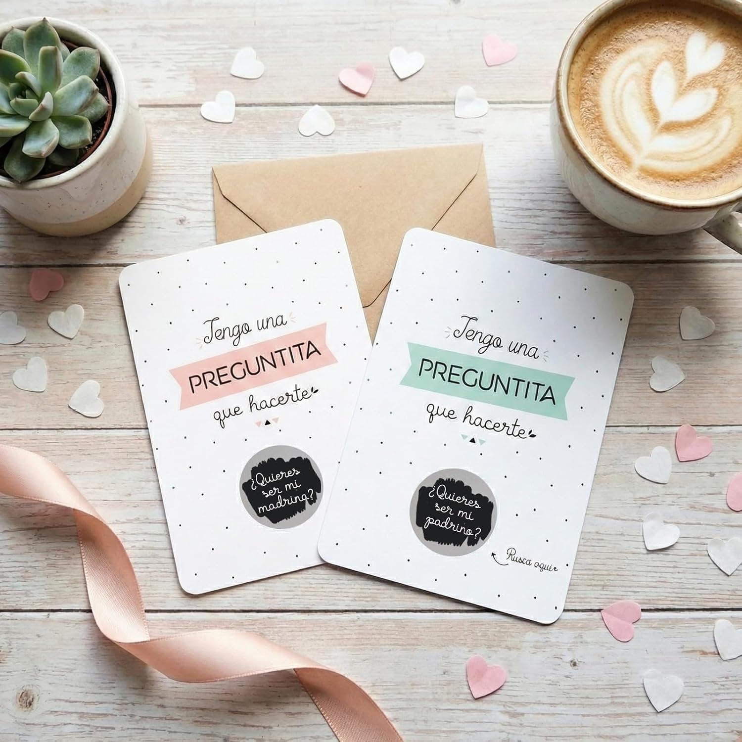 Las dos tarjetas sobre una mesa de madera clara con un sobre kraft, un café y confeti de corazones alrededor