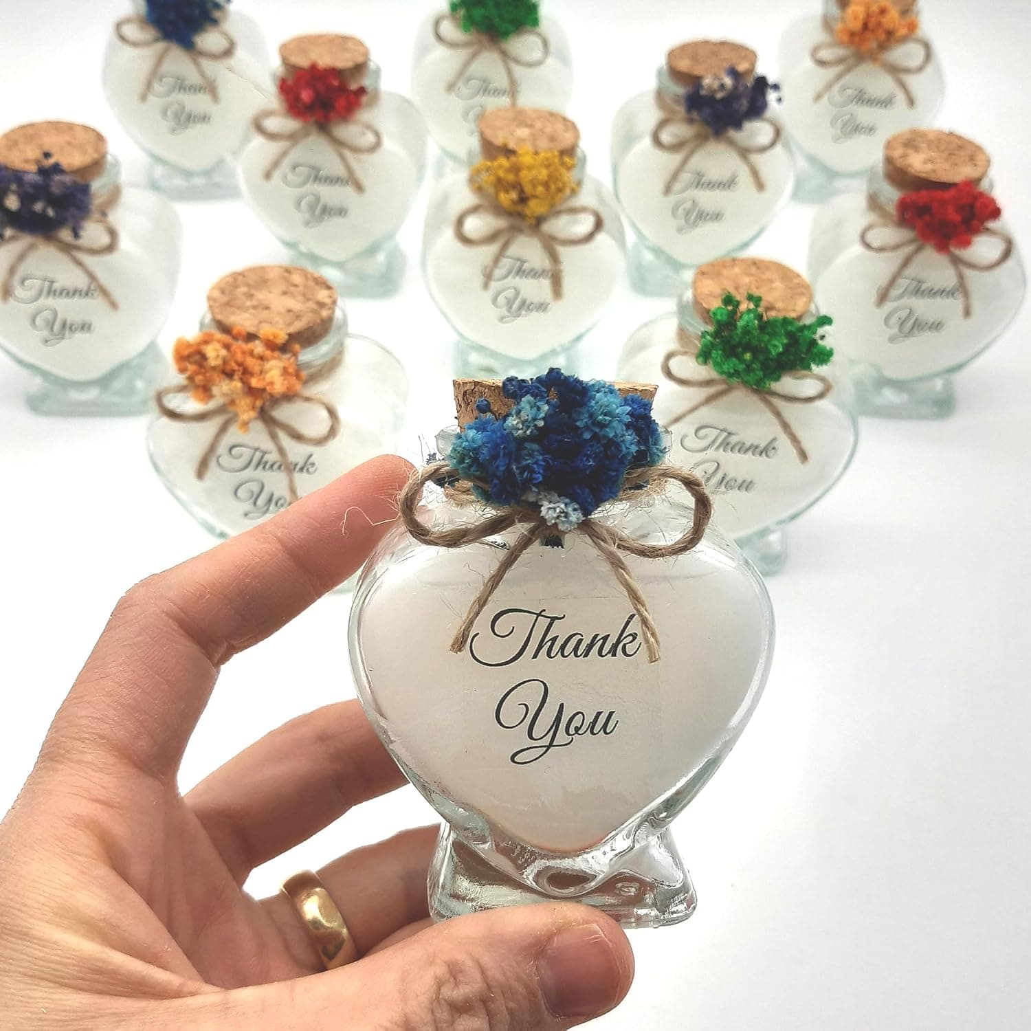 Fila de botellas de cristal con velas y flores secas, cada una con su lazo de rafia y su corcho