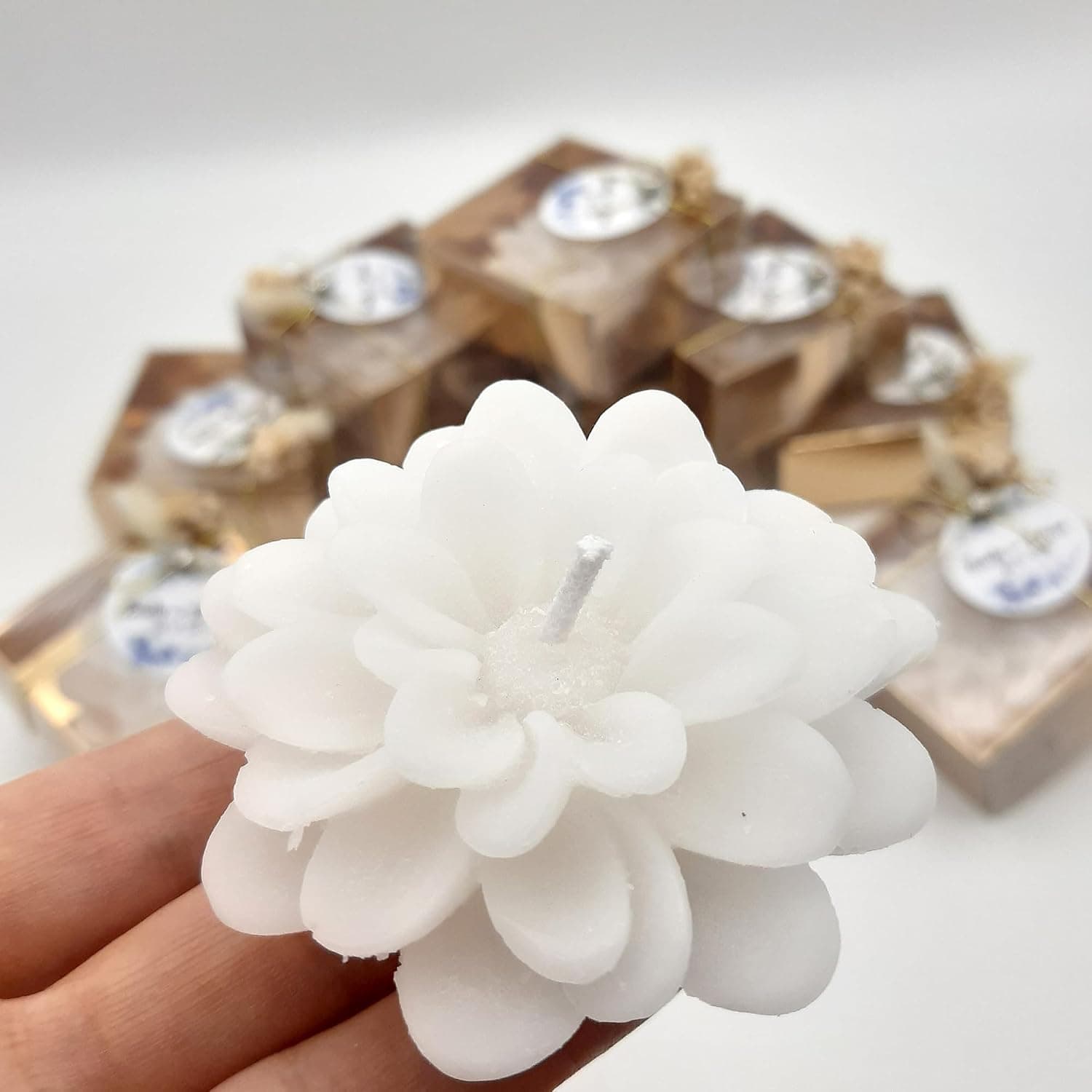 Cajita transparente con tono dorado que contiene la vela con forma de flor, cerrada con hilo dorado y una etiqueta redonda con los nombres de los novios y la fecha