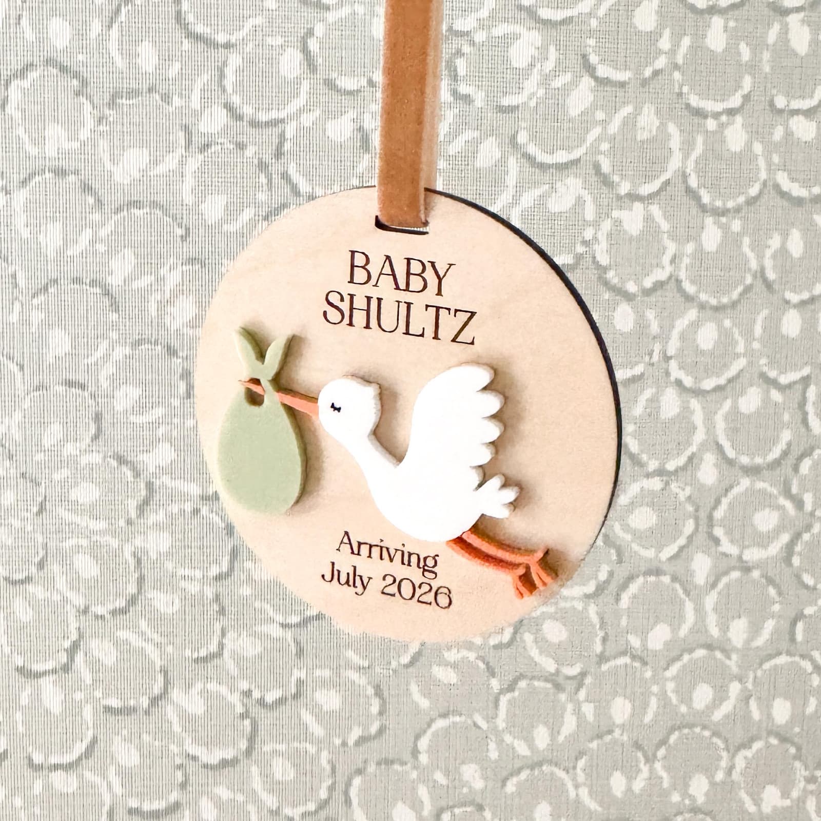 Layered wood and acrylic baby announcement ornament. Personalize with baby’s last name and arrival month and year. Features a white acrylic stork and customize with your choice of acrylic color for stork bag.