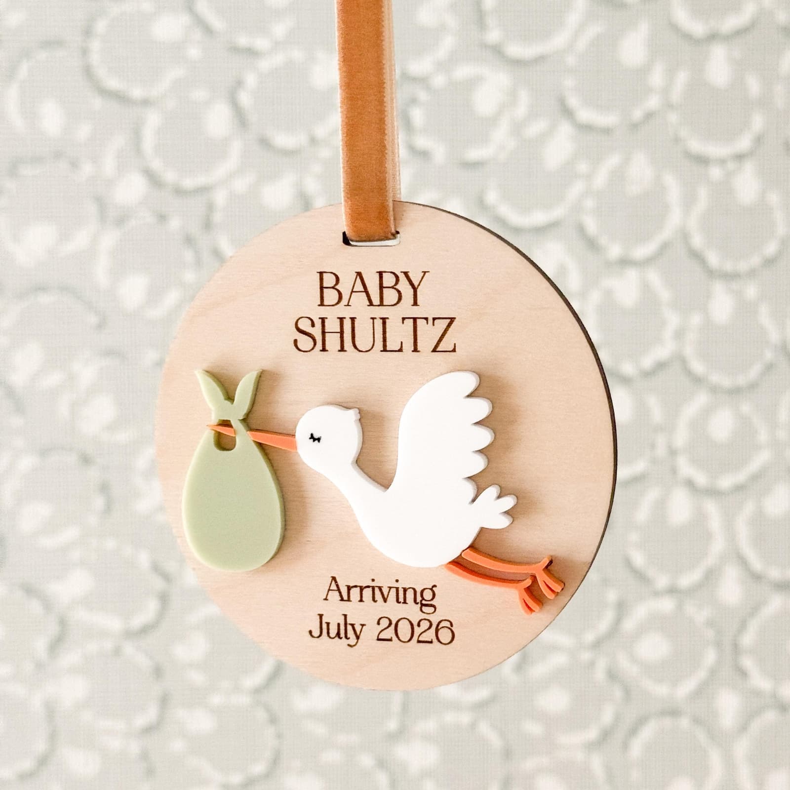 Layered wood and acrylic baby announcement ornament. Personalize with baby’s last name and arrival month and year. Features a white acrylic stork and customize with your choice of acrylic color for stork bag.