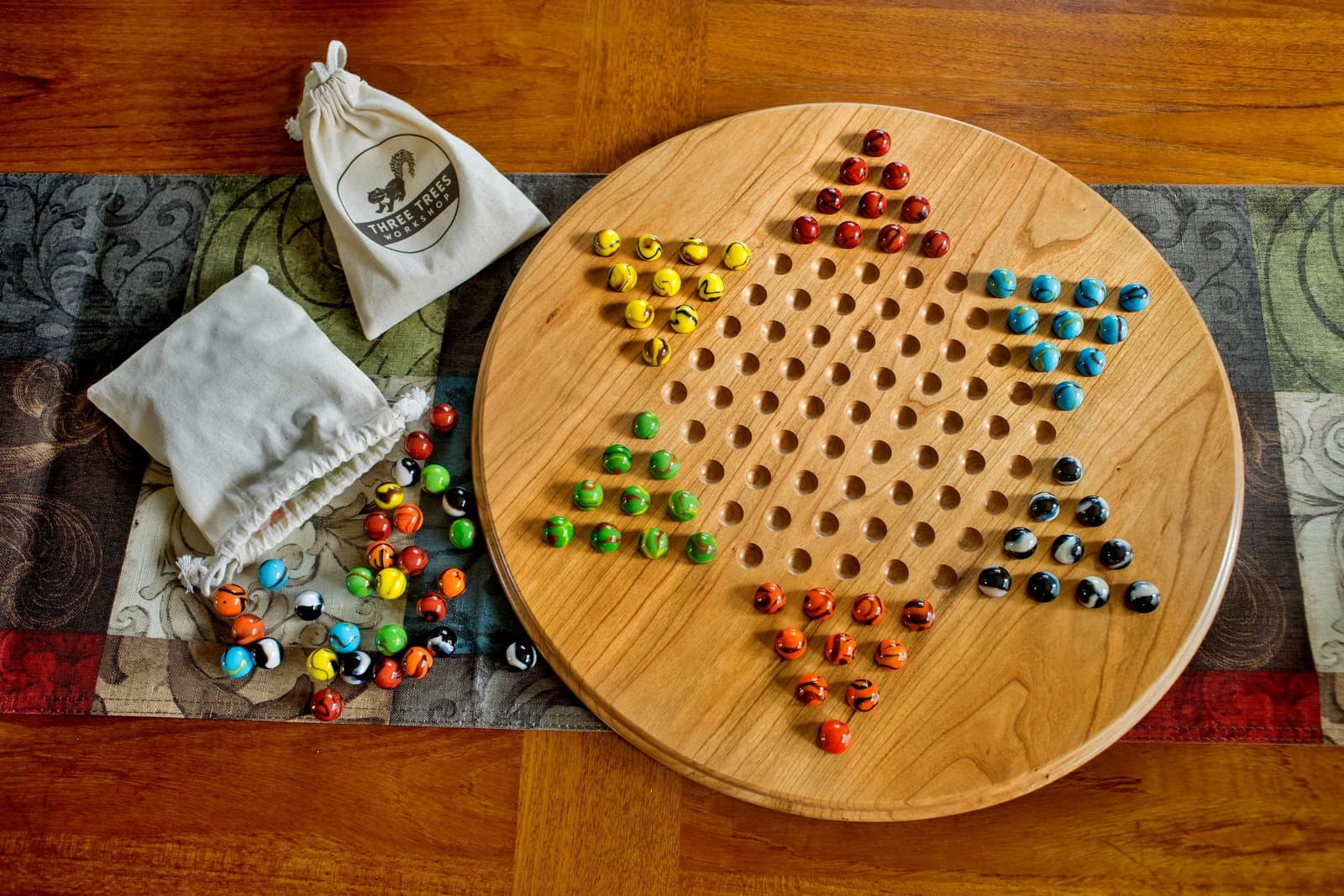 Tablero en madera clara de acabado natural con canicas de seis colores listas para jugar