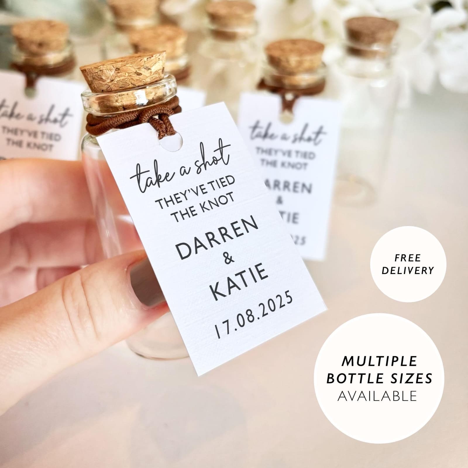Botellitas de cristal con tapón de corcho y etiqueta «Take a shot, they've tied the knot», con los nombres de los novios y la fecha