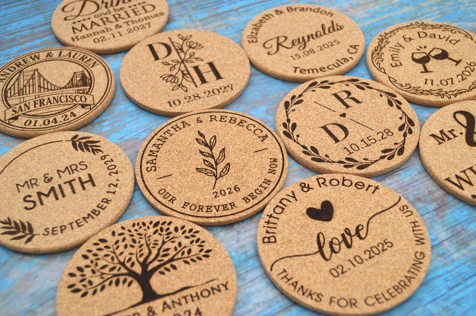 Posavasos redondos de corcho natural con distintos grabados, ramas y nombres de parejas, colocados sobre una mesa de madera