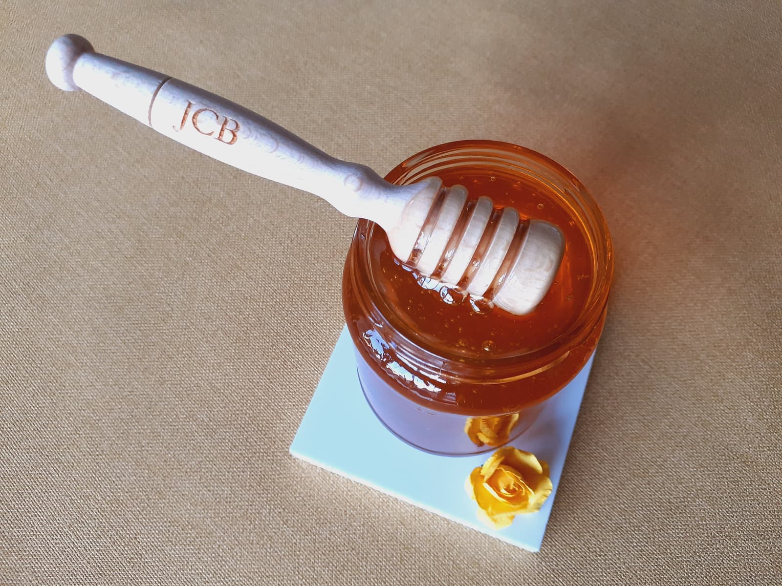 Cuchara de miel de madera grabada con iniciales, apoyada sobre un tarro de miel