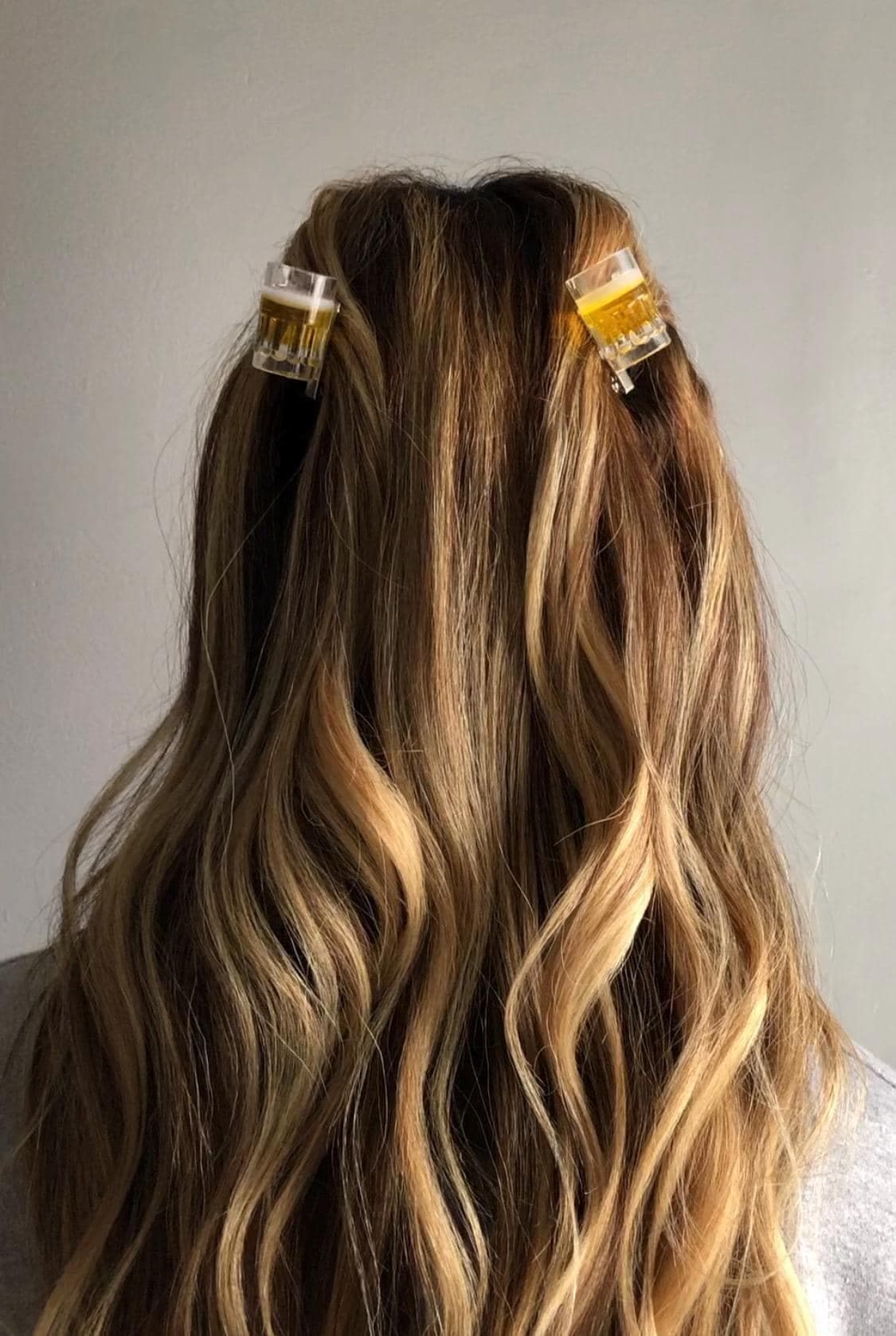 May include: Two clear hair clips with a yellow liquid inside. The clips are in a person's hair.