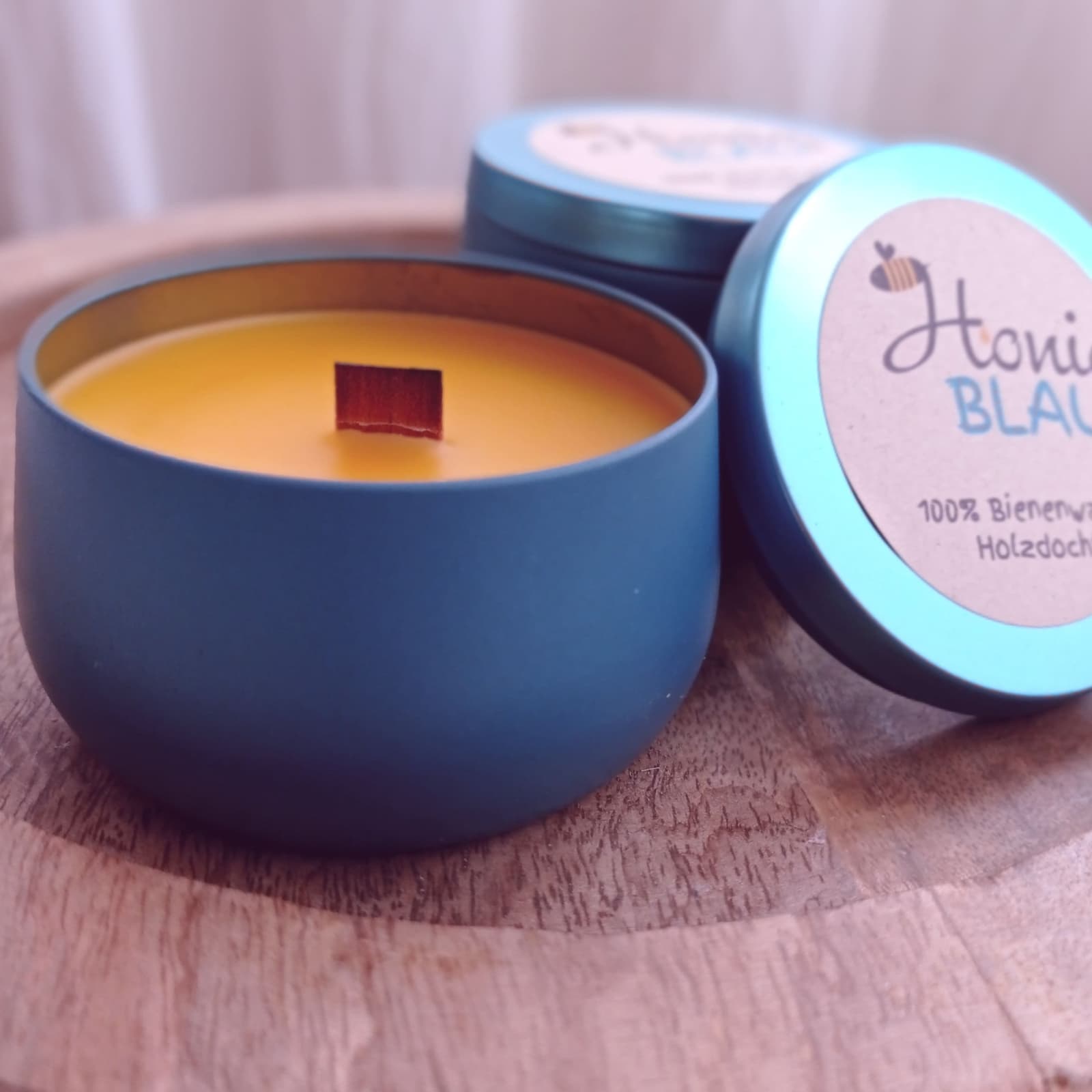 Vela de cera de abeja encendida dentro de una lata metálica azul, con mecha de madera crepitando