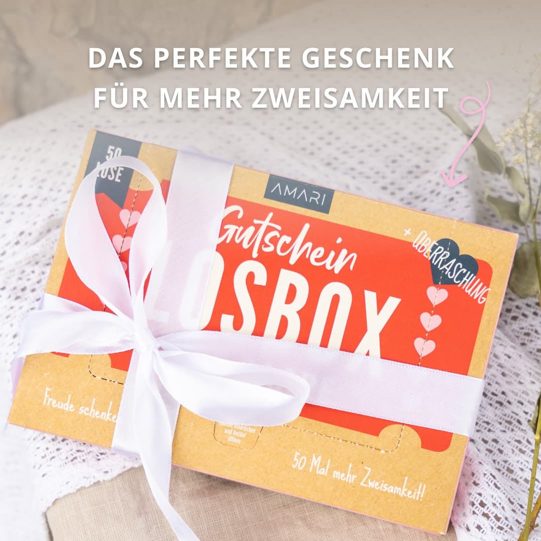 AMARI Gutscheinbox, geschmückt mit Schleife auf einer Decke – das perfekte Geschenk für mehr Zweisamkeit und gemeinsame Freude.