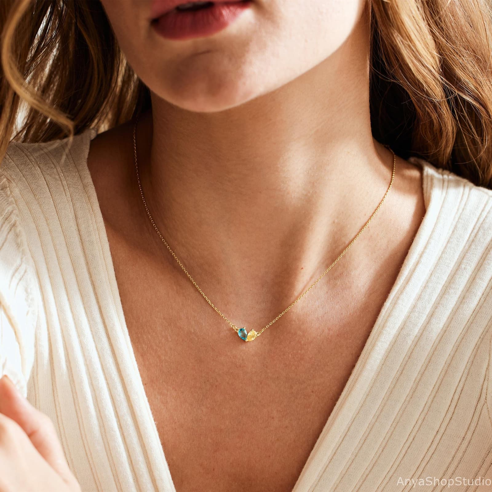 May include: A fine gold necklace with two small gemstone pendants. One pendant is teal, the other yellow. The necklace is shown against a white ribbed top. The gemstones are likely small, measuring a few millimetres.