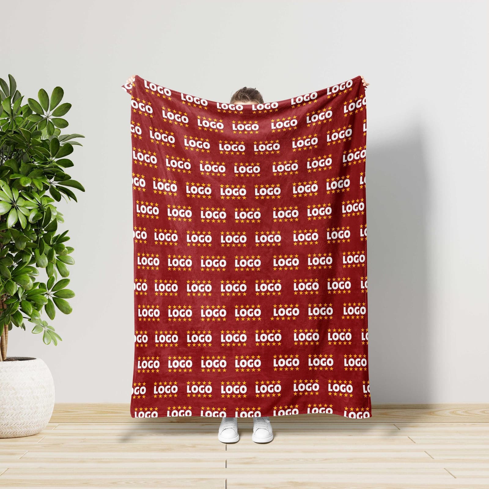 A person is standing in front of a red blanket with a repeating pattern of the word "LOGO" on it.