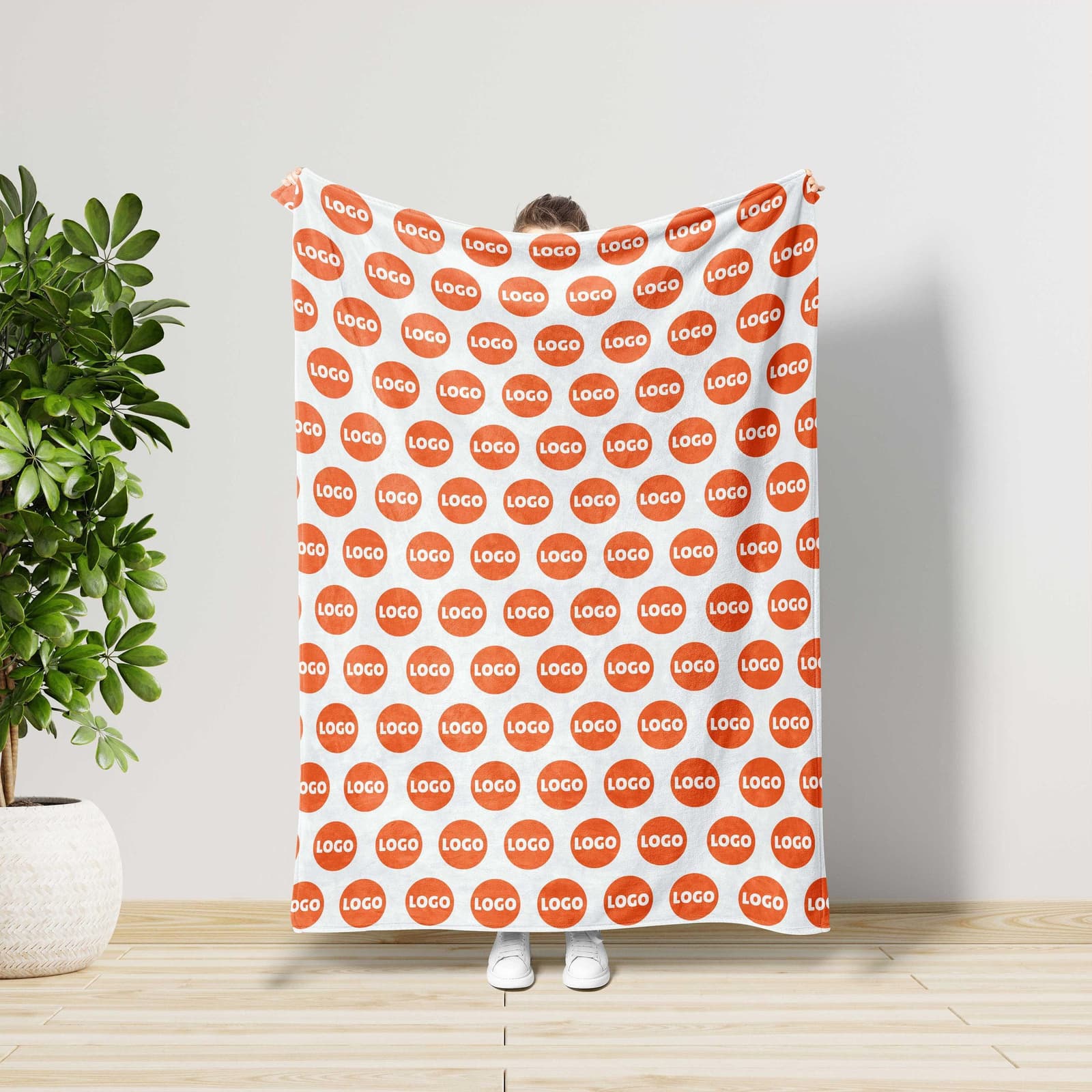 A person is standing in front of a white wall, holding a large blanket with a repeating pattern of orange circles.