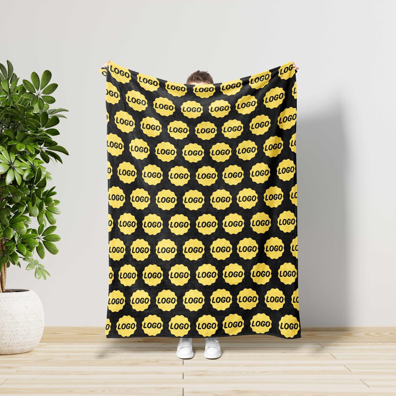 A person is standing in front of a black and yellow patterned blanket, holding it up to their face.