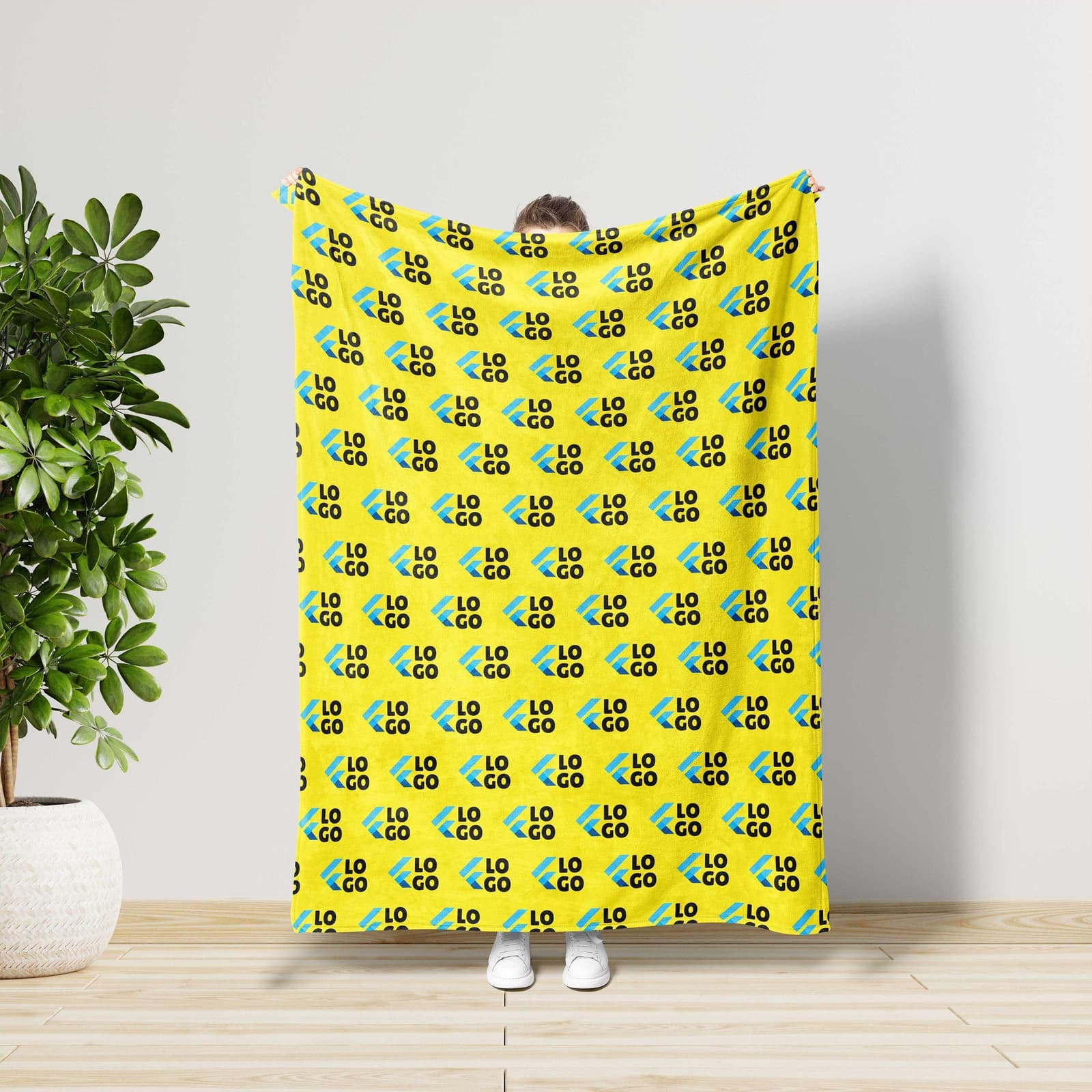 A person is holding up a yellow blanket with a repeating pattern of the word "LO" in black and blue colors.
