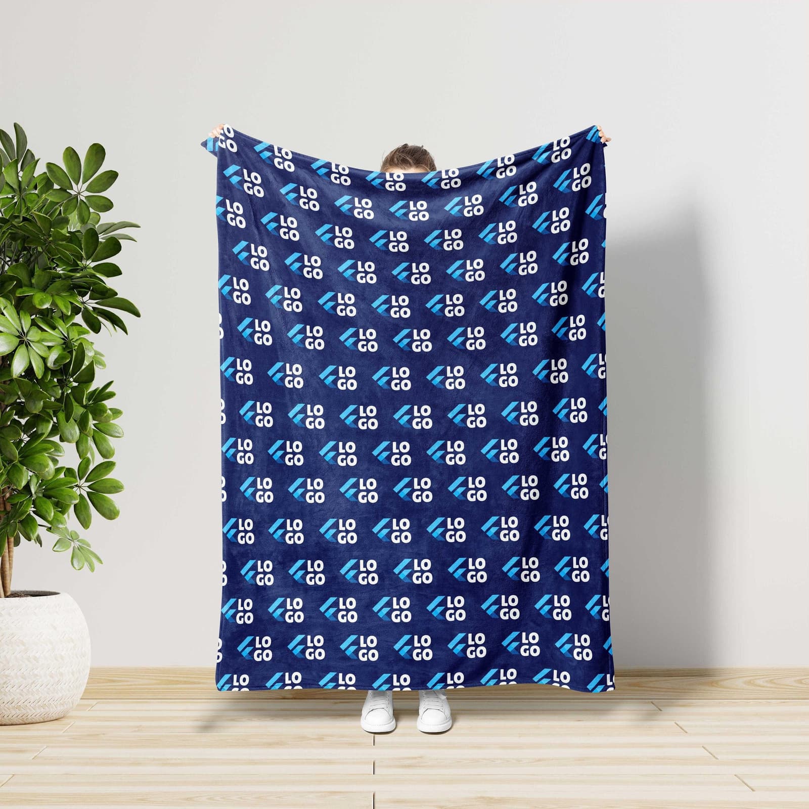 A person is holding up a blue blanket with a repeating pattern of the letters "LO" in white, which appears to be a logo or design.