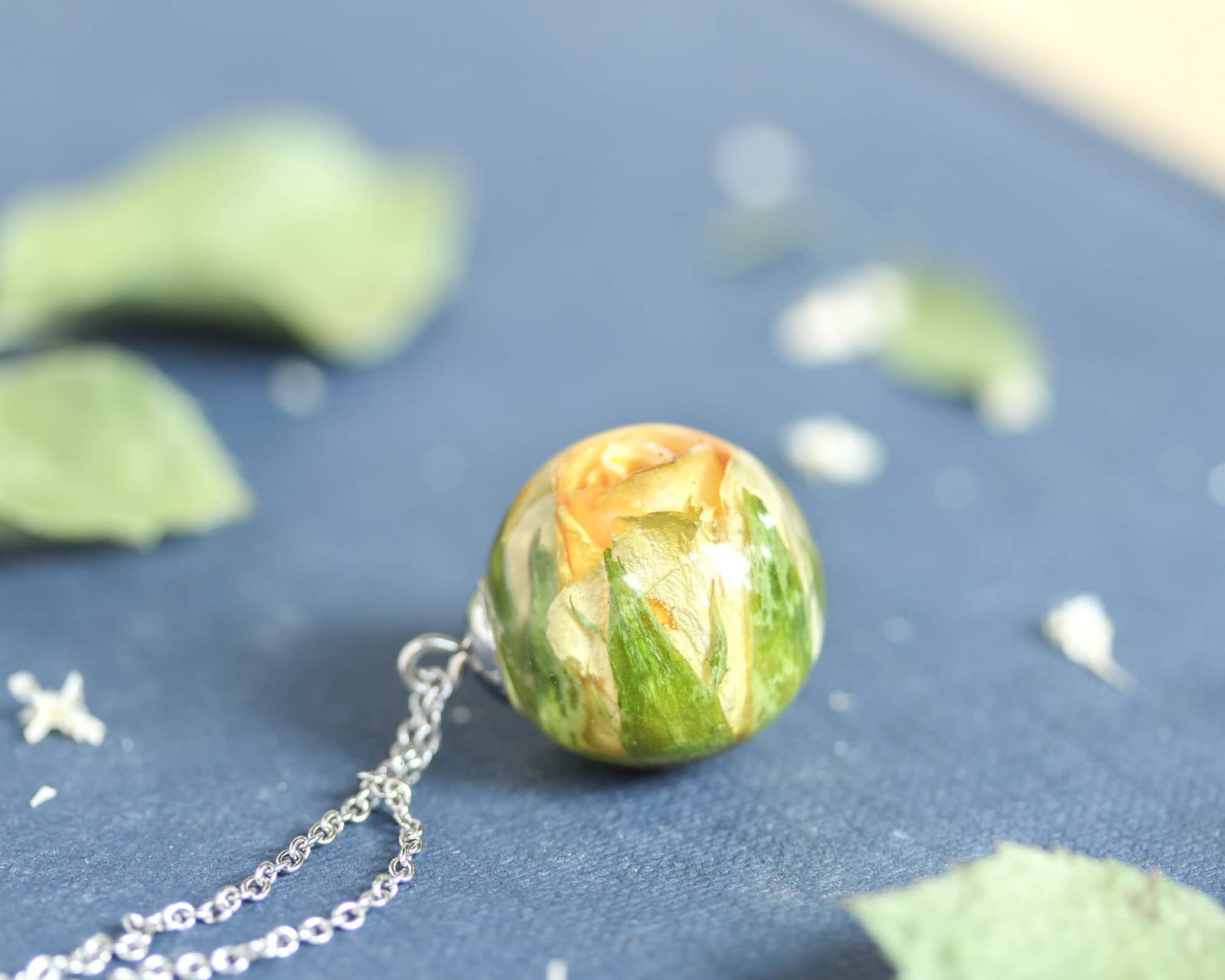 Side view of the yellow rose resin pendant showing the layered petals and leaves inside the clear resin sphere.