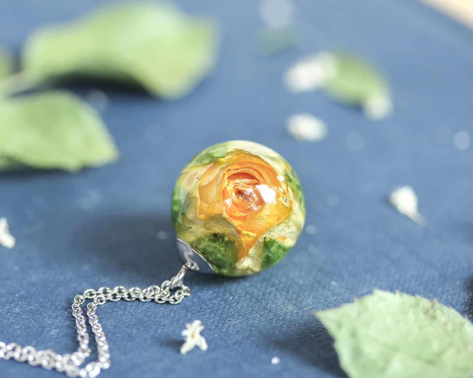 Detailed view of a yellow rose preserved inside a handmade resin orb pendant on a silver chain.