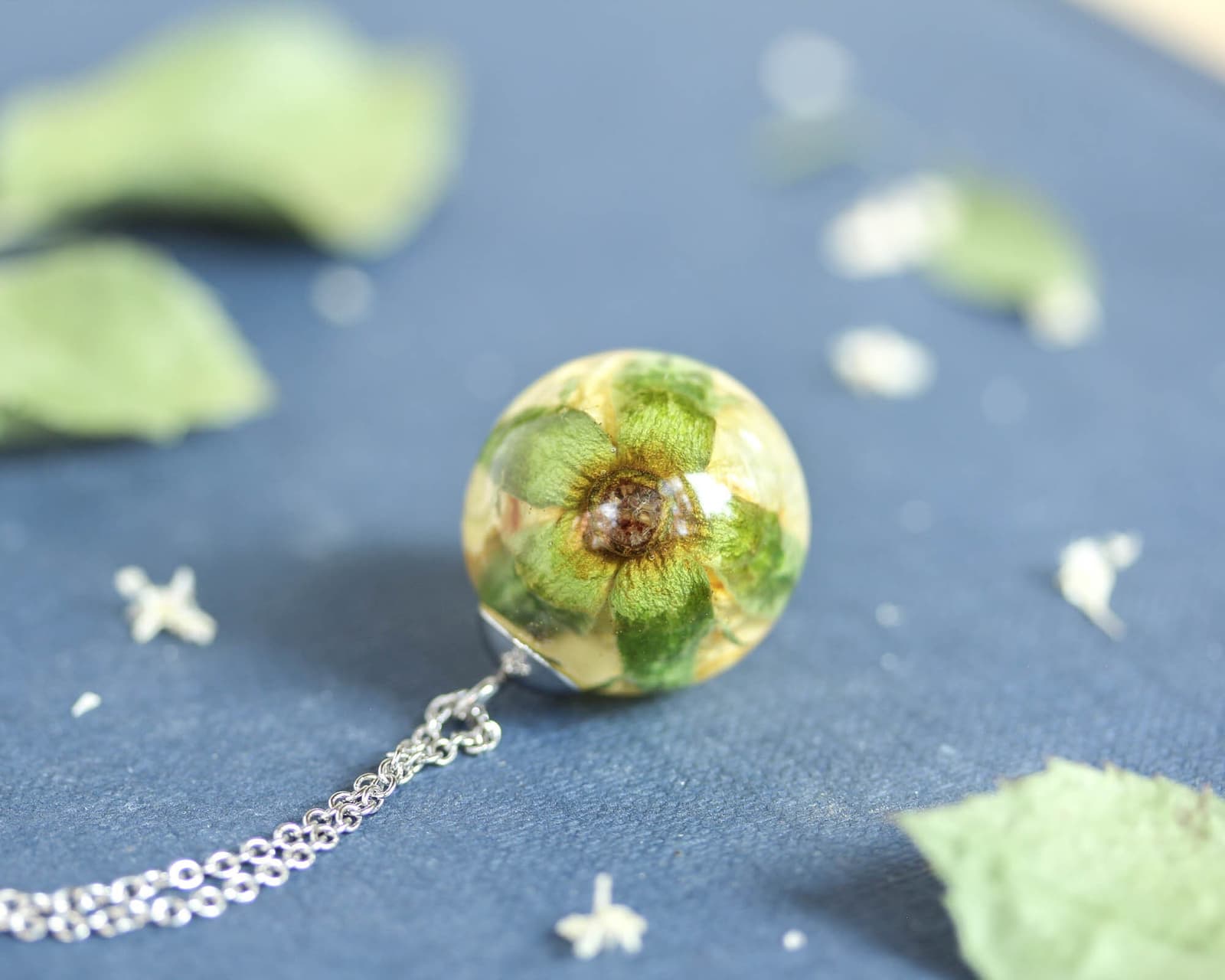 Bottom view of the yellow rose resin pendant, showing the preserved green sepal details inside the round resin orb.