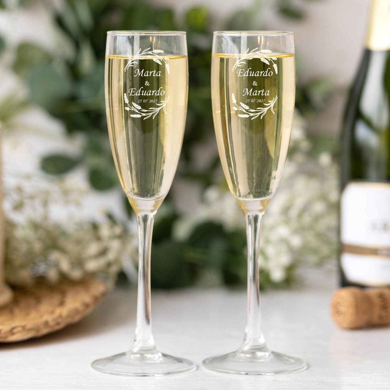 Las dos copas servidas sobre una mesa, con una botella de cava y flores al fondo