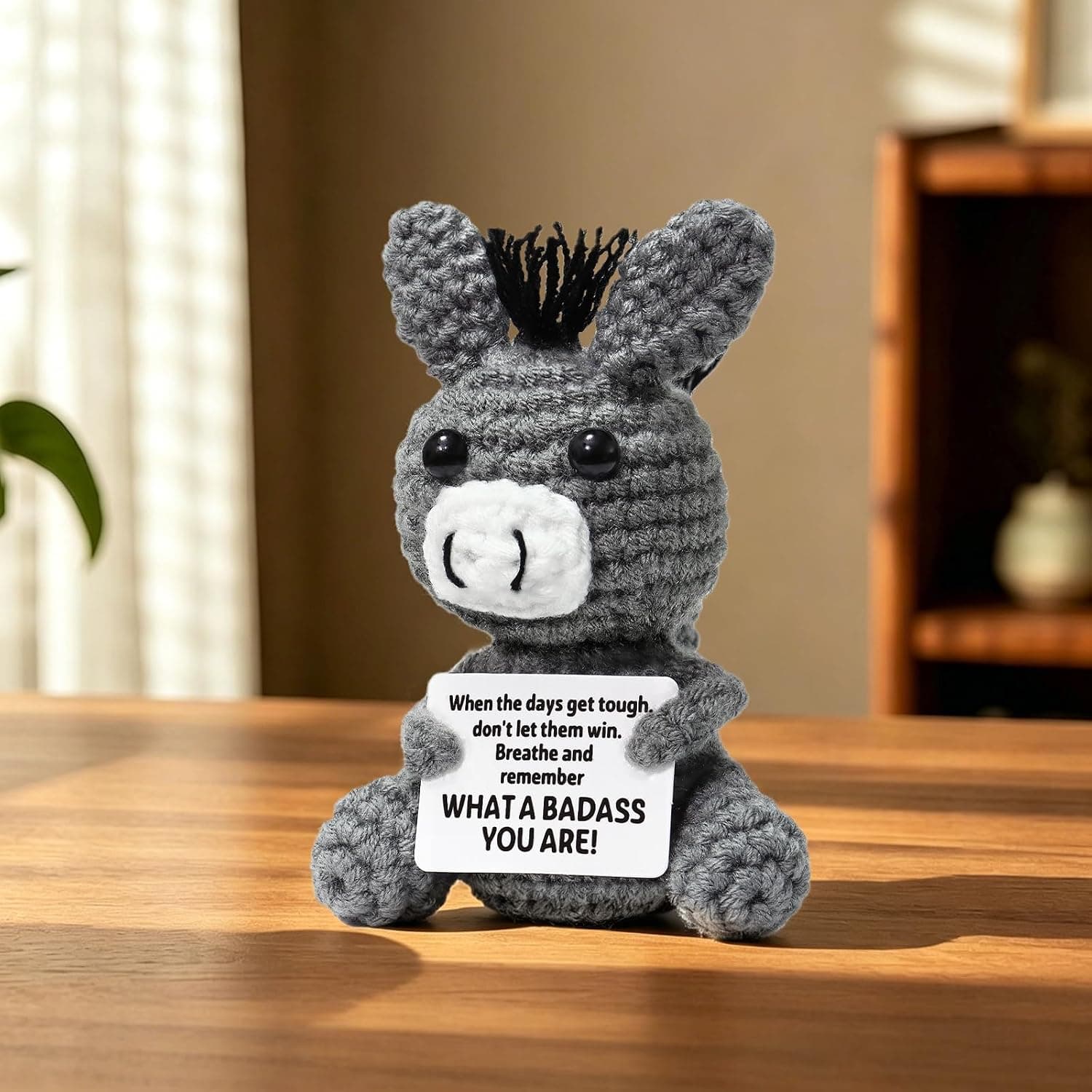 Peluche de ganchillo gris con forma de burrito, orejas largas y crin negra, sosteniendo una tarjeta con el mensaje en inglés
