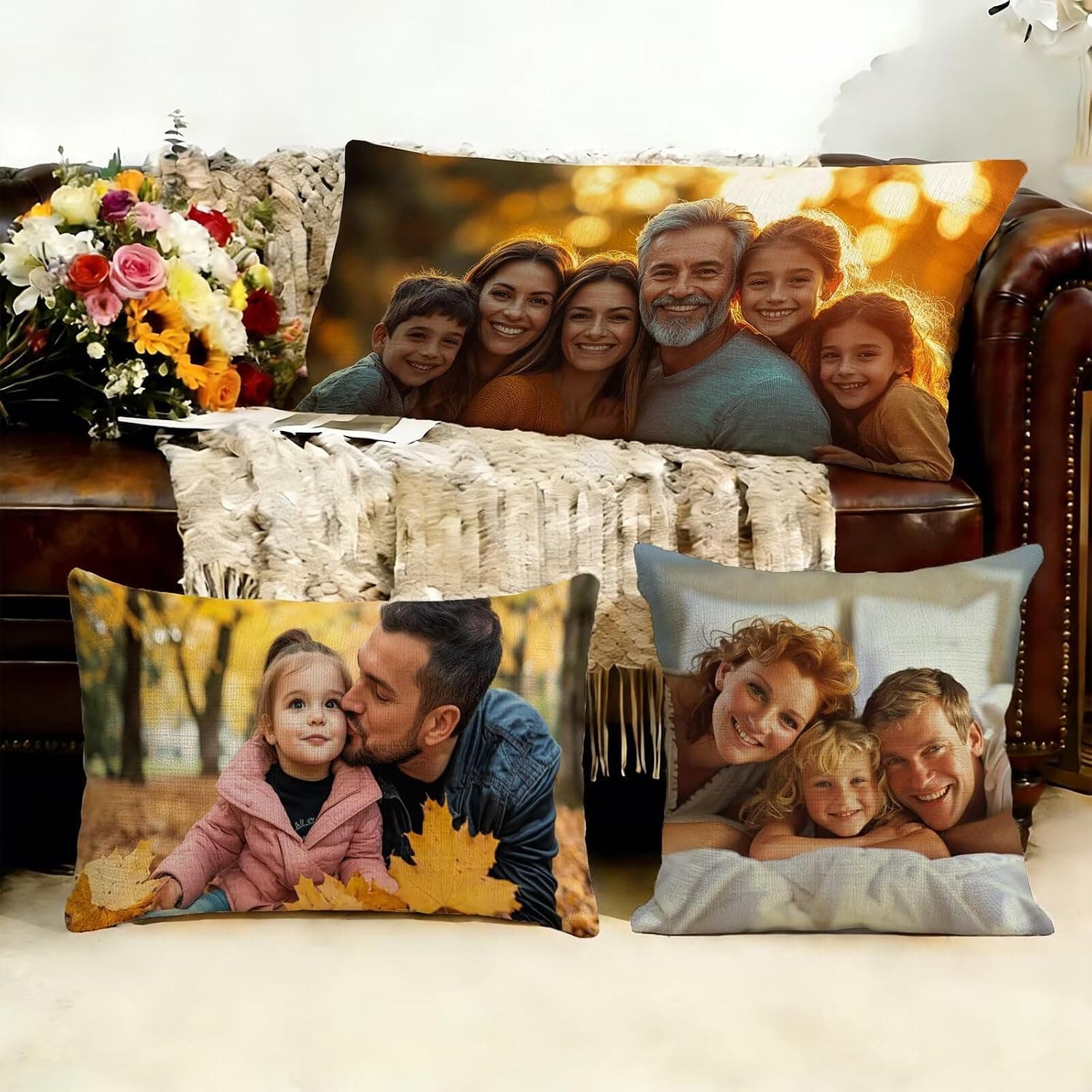 Tres cojines alargados con distintas fotos familiares impresas, colocados sobre un sofá de cuero junto a un ramo de flores