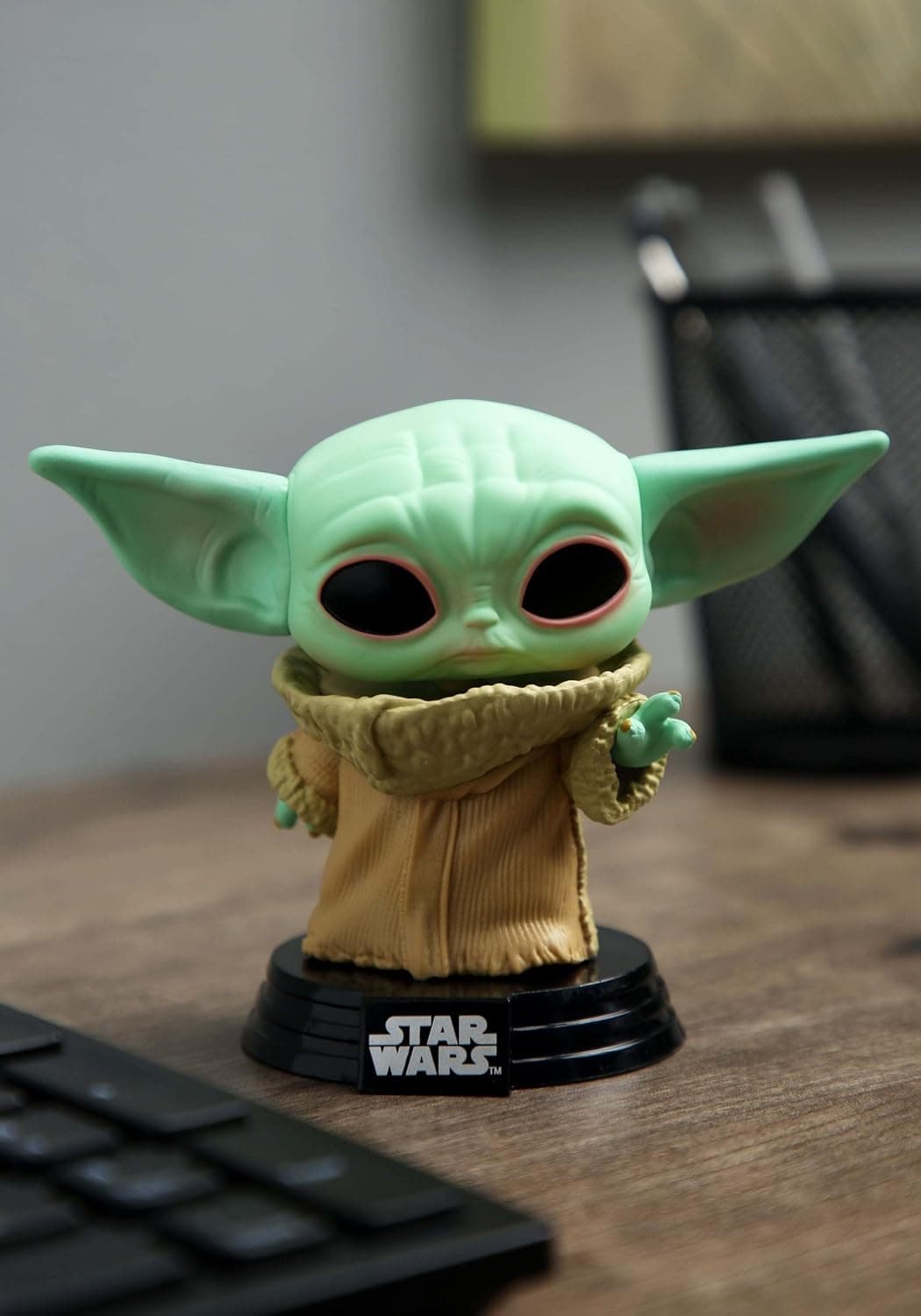 La figura de Grogu con su túnica marrón, de pie sobre la peana negra de Star Wars, junto a un teclado