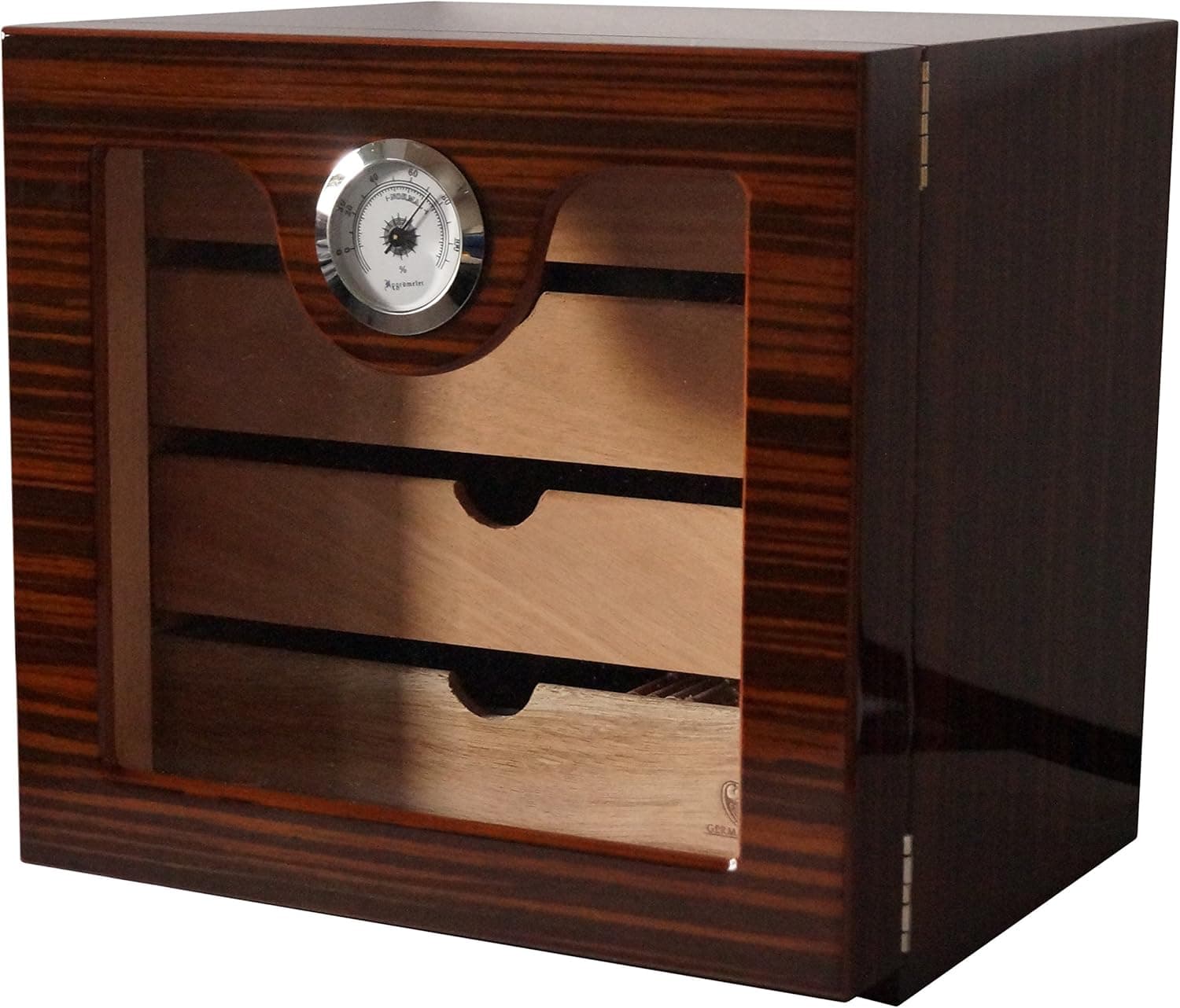 El humidor cerrado, con el exterior de veta oscura brillante, la ventana de cristal y el higrómetro redondo sobre el primer cajón