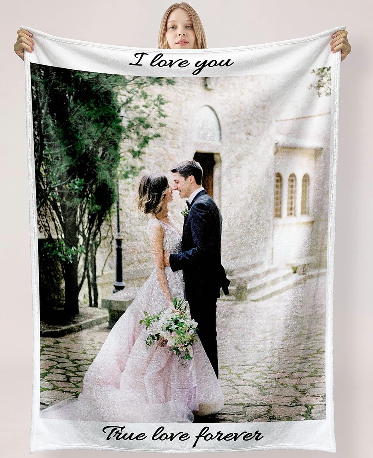 Manta blanca con la foto de una pareja de novios abrazados y los textos "I love you" y "true love forever" impresos arriba y abajo, sostenida por una mujer