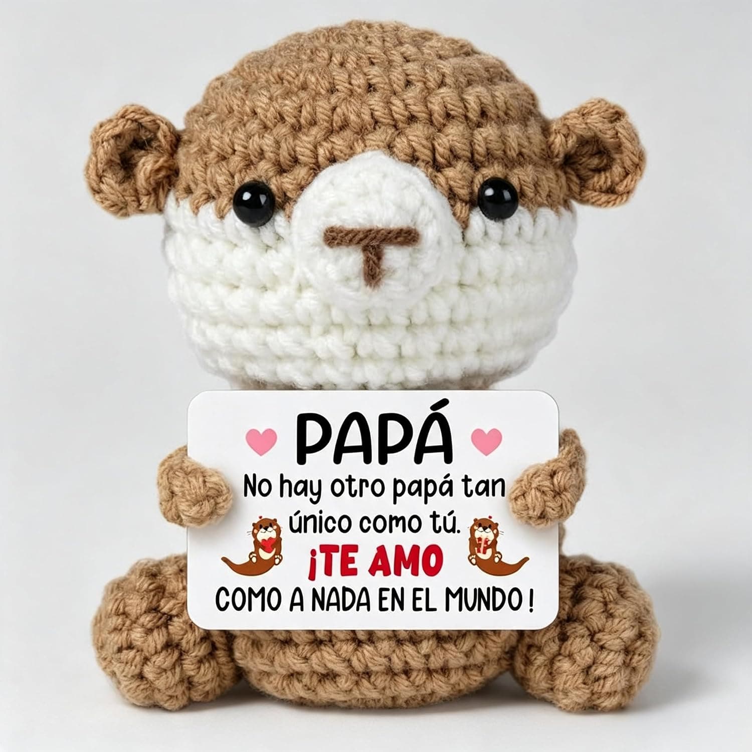 Peluche de ganchillo marrón y blanco con forma de nutria, sosteniendo una tarjeta con el mensaje para papá