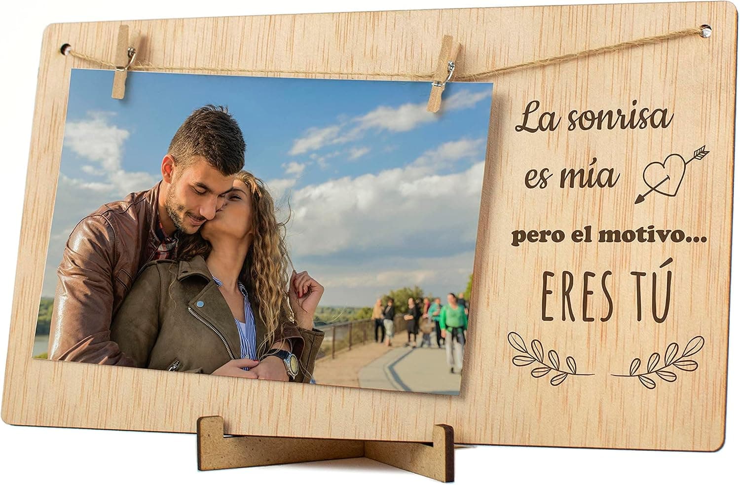 La tabla de madera con una foto sujeta por una pinza y la frase impresa al lado, apoyada junto a unas flores amarillas y una vela