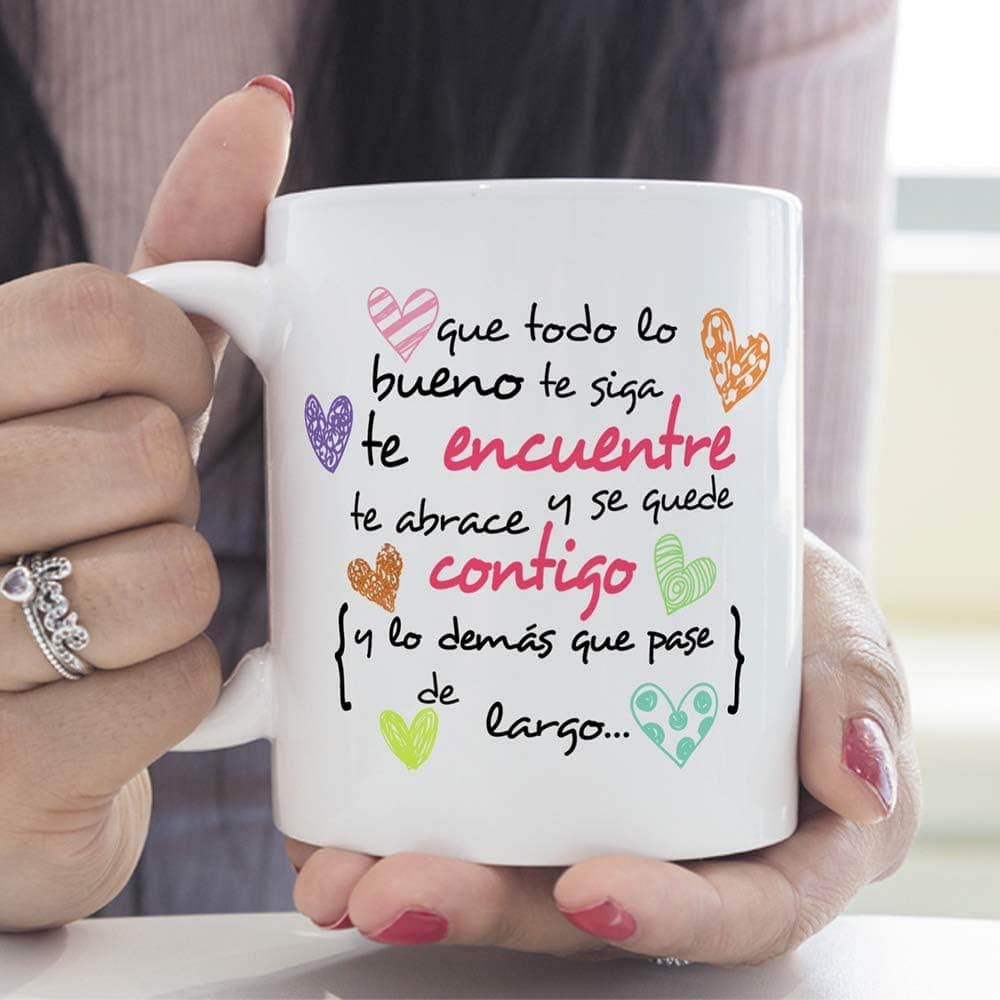 Taza blanca vista de frente con la frase «que todo lo bueno te siga, te encuentre, te abrace y se quede contigo, y lo demás que pase de largo» escrita a mano en morado, rosa y verde, con corazones sueltos