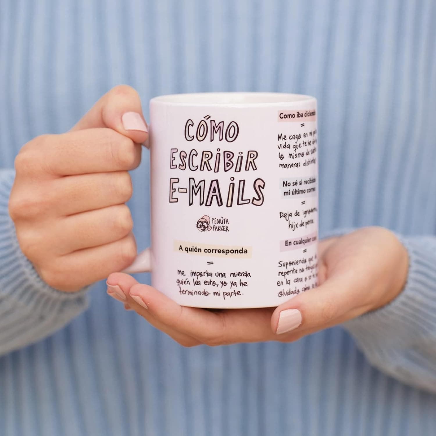 Dos manos sostienen la taza rosa claro con el título «Cómo escribir e-mails» y una columna de fórmulas de correo con su traducción debajo, en letra manuscrita