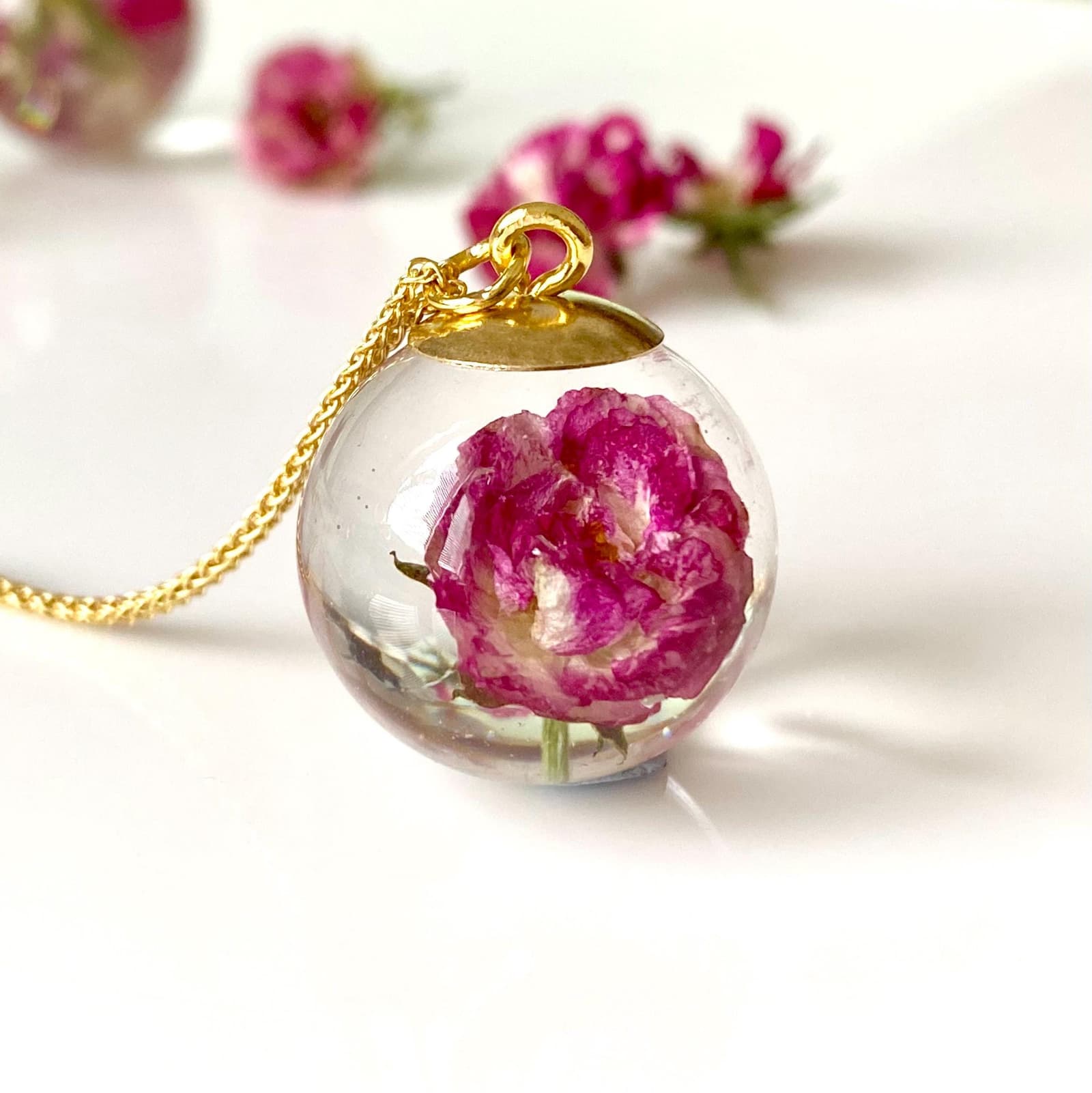clear resin orb with a pinky red rose inside on a gold chain
